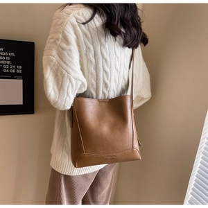 Dettaglio di una borsa a secchiello in pelle marrone con logo e texture opaca