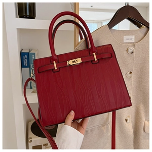 Close-up of deep red wave-textured leather handbag with golden twist lock and metal hardware