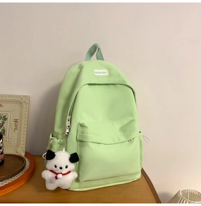 Detail of light green canvas backpack with a cute white plush dog charm on the zipper