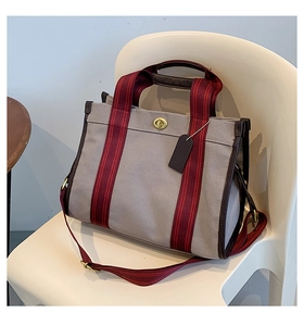 Detail of taupe canvas tote with red-brown striped handles and gold twist lock closure