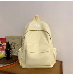 Detail of light yellow nylon backpack showing front zipper pocket and BOKA BAG logo label