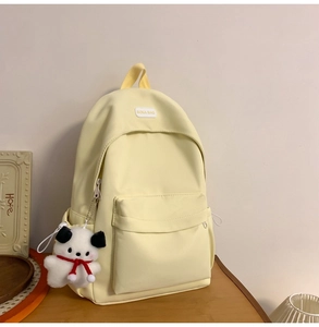 Close-up of a light yellow nylon backpack featuring a cute puppy plush charm and logo