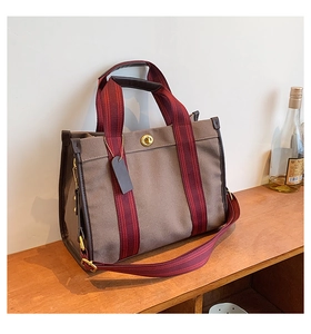 Detail of canvas tote bag with burgundy webbing straps and iconic metal turn-lock closure