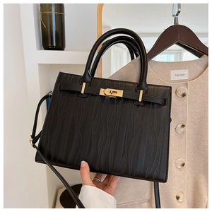 Detail view of black textured leather handbag with gold twist-lock and top handles