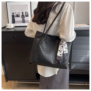 Macro detail of black houndstooth embossed tote bag with woven straps and cherry silk scarf