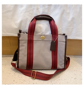 Close-up of canvas tote bag featuring leather trim, red striped straps, and gold twist lock