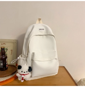 Close-up of white minimalist backpack with brand logo and cute plush dog charm