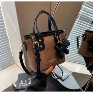 Detail of a brown textured bucket bag with black leather handles and dog charm