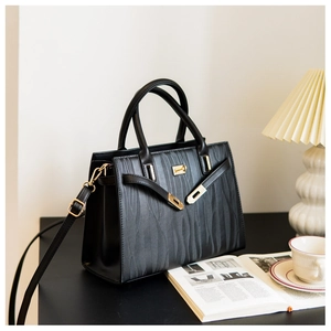 Detail of black wave-pattern leather handbag with gold buckle and crossbody strap