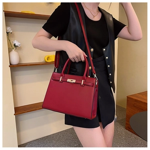 Detail of red leather luxury handbag with gold twist lock worn with black leather outfit