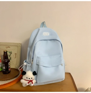 Detail of light blue nylon backpack with BOKA BAG label and cute white dog charm accessory