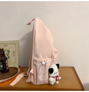 Side view of pink canvas backpack with side pocket and a cute puppy plush charm accessory
