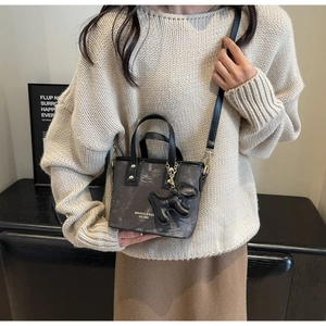 Close-up of the mini bucket bag with textured print, leather handles and a doll charm