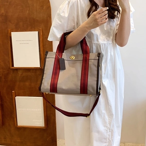 Canvas tote bag with red stripes and leather trim shown in a stylish crossbody wear
