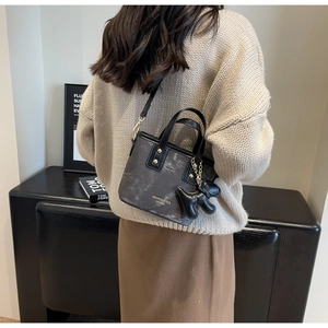 Detail of grey marble bucket bag with plush dog charm worn over a beige sweater