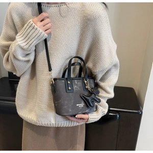 Detail of dark grey textured bucket bag with shoulder strap and cute dog charm on model