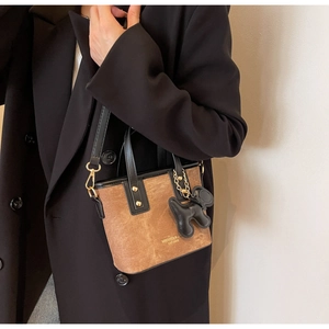 Brown suede bucket bag detail with black puppy charm and gold hardware on black coat