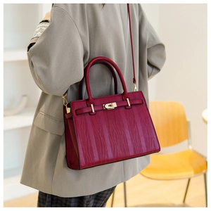 Detail of burgundy textured leather handbag with gold metal clasp on gray suit