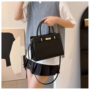 Modern black handbag with golden metal lock shown on a model in a minimal interior