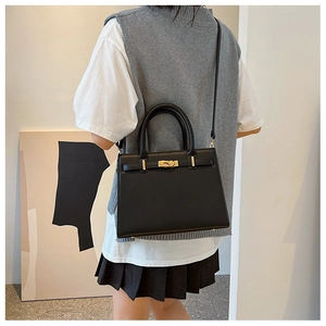 Elegant black matte leather handbag with metal lock shown as a crossbody on a model