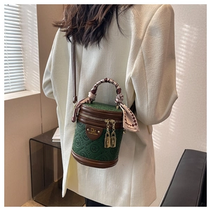 Detailansicht einer dunkelgrünen Zylindertasche mit Seidenschal-Griff und Goldschlössern