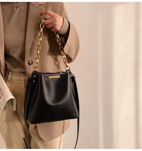 Dettaglio borsa a secchiello nera in pelle con catena dorata spessa e fibbia metallica elegante