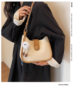 Detail of a beige and brown saddle bag with a furry monster charm on a black coat