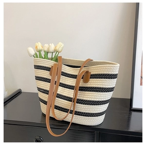 Detailed view of woven straw tote bag with black wavy stripes and leather handles