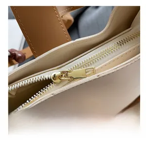 Detail of smooth gold-tone zipper and beige leather texture on crossbody bucket bag