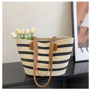 Detail of woven straw tote bag with black horizontal stripes and brown leather handles