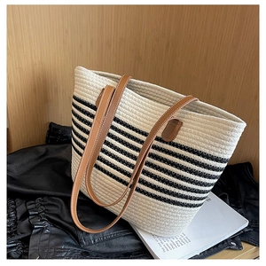 Detail of striped straw tote bag featuring brown leather handles on rustic background