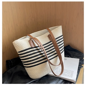 Detail of woven straw tote bag with classic black stripes and brown leather handle