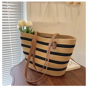 Close-up of woven straw tote bag with black stripes and premium leather handles