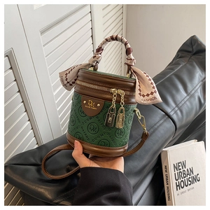 Detail der grünen Bucket-Bag mit Logo-Prägung und Seidenschal am geflochtenen Griff