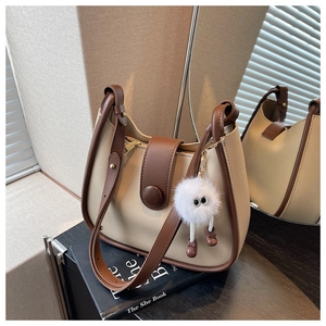Detail of beige and brown crossbody bag with a fuzzy monster charm and gold zipper