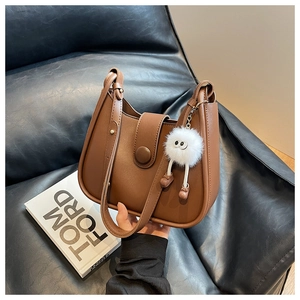 Detailed close-up of brown matte leather bucket bag with white plush monster charm on sofa