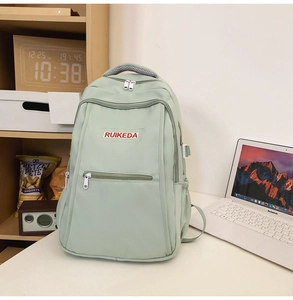 Detail of mint green nylon backpack with front zipper pocket and padded top handle