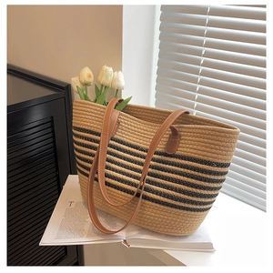 Detail of woven straw tote bag with black stripes and brown leather handle on a windowsill