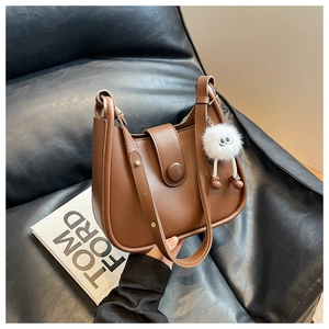 Brown leather crossbody bucket bag with white furry monster charm on black leather sofa