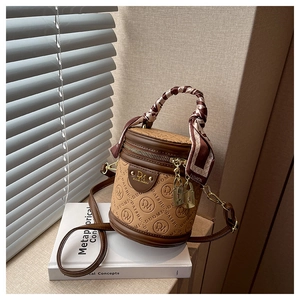 Detail der braunen Zylindertasche mit Monogramm-Prägung und seidenumwickeltem Griff
