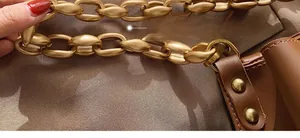 Dettaglio della catena dorata opaca sul manico di una borsa a secchiello marrone