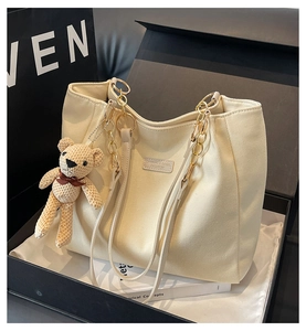 Close-up of beige canvas tote bag with gold chain strap and bear charm in a gift box