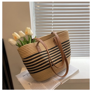 Detail of woven straw tote bag with black stripes and leather handles on windowsill