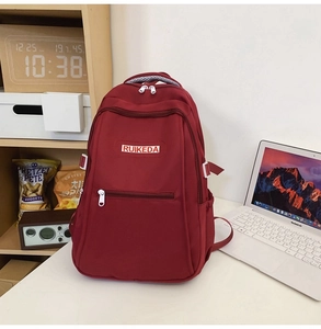Close-up of a burgundy canvas backpack with RUIKEDA logo and multi-pocket zippers