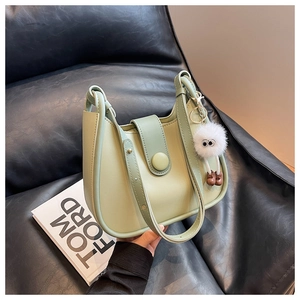 Detail of green leather shoulder bag with dark green flap and plush doll accessory