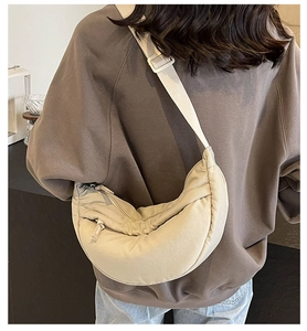 Back view of a beige crescent nylon crossbody bag on a model in a minimalist setting