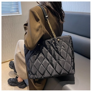 Fashionable black quilted nylon tote bag with elegant chain straps worn by model