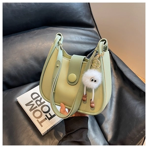 Detail view of light green crossbody bucket bag with cute plush monster charm on leather sofa