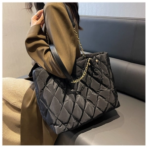 Detail of black quilted nylon tote bag with golden metal chain strap on leather sofa