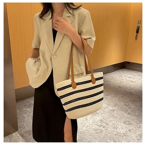 Close-up of woven straw tote bag with black stripes and brown leather shoulder straps